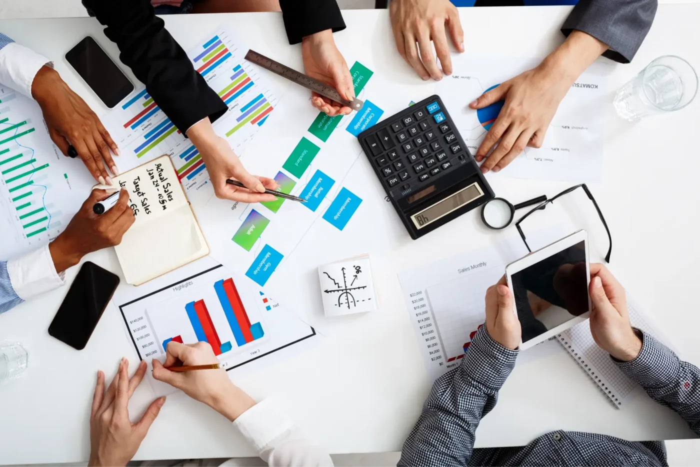 Hands above table interacting with a tablet and calculator while reviewing charts