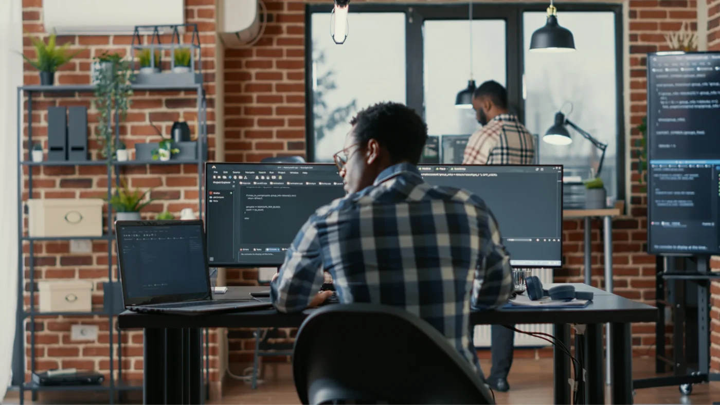 Programmer coding on their laptop with two monitors